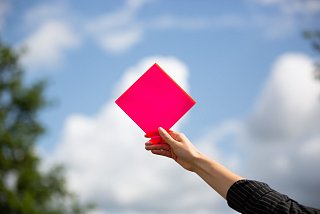 Eine Hand hält eine rote Raute in den Himmel