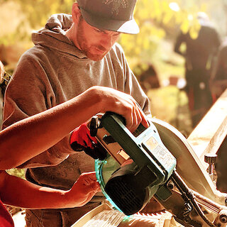 Männer arbeiten mit einer Säge an einem Balken Holz