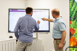 Zwei Männer im Büro zeigen auf einen Bildschirm mit einem Fließbild